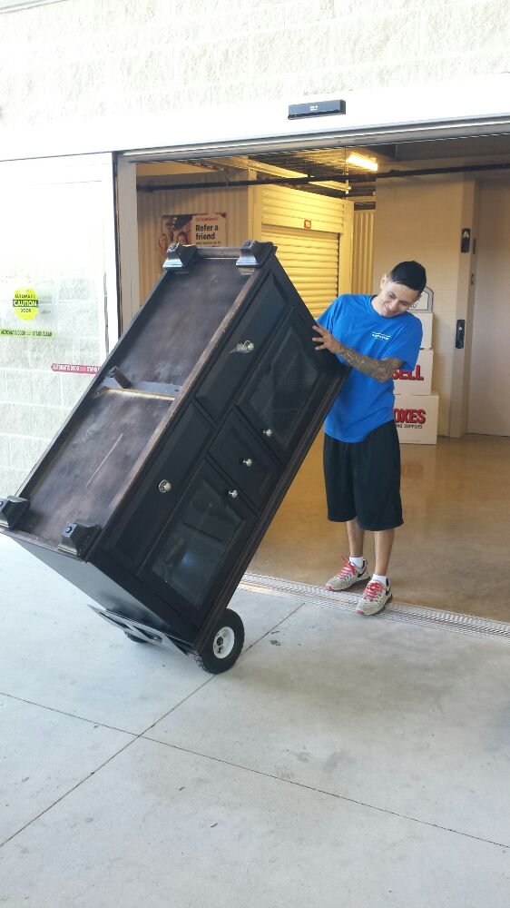 Mover transporting a dresser on a dolly at a storage unit
