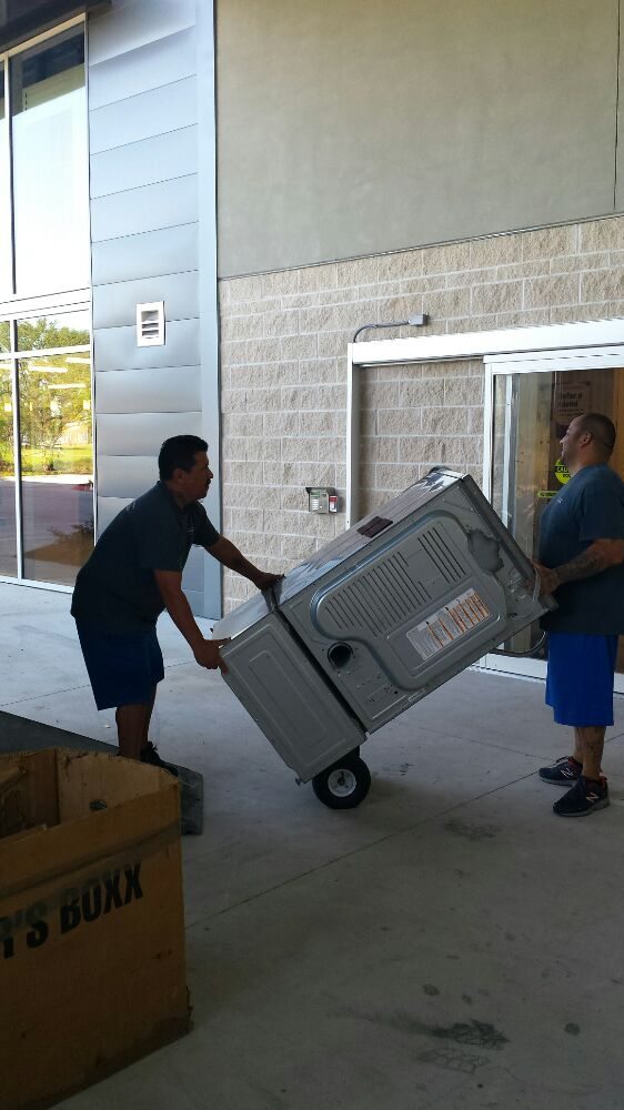 Two movers carefully rolling an appliance on a dolly